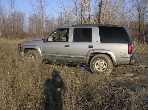 2000 Chevrolet Tahoe - This silver SUV is stuck in a muddy field, with its tires partially submerged in the mire.