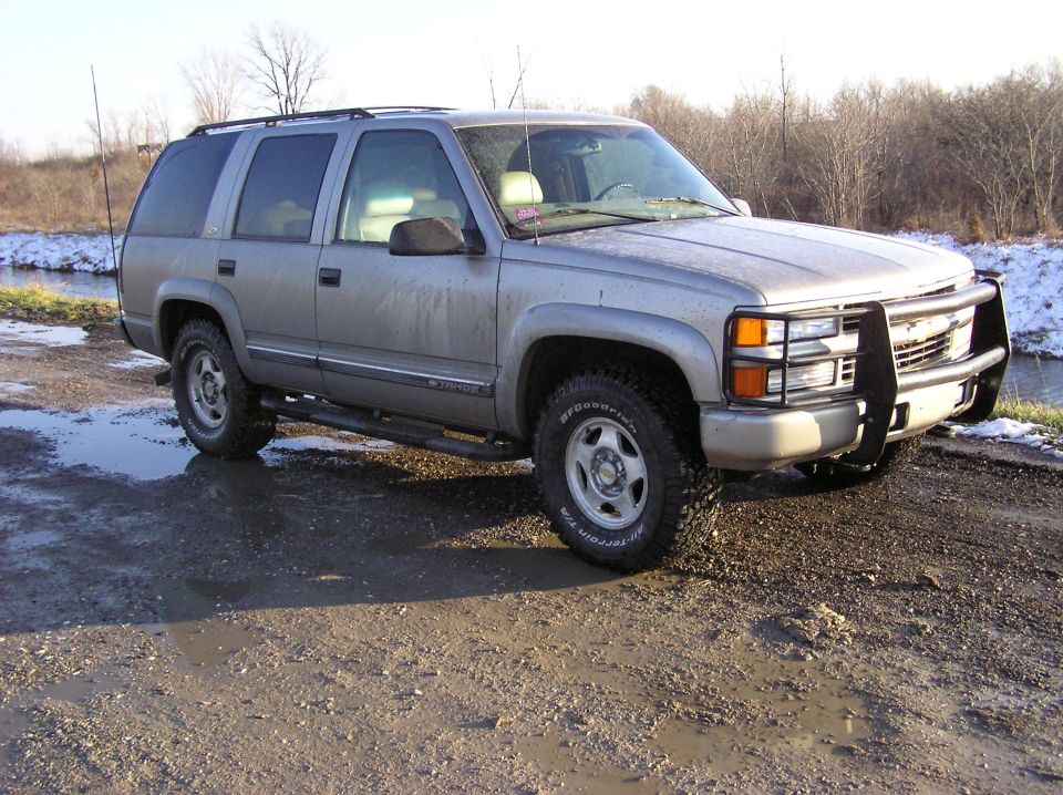 Silver Chevrolet Tahoe with a brush guard and running boards parked on a muddy road