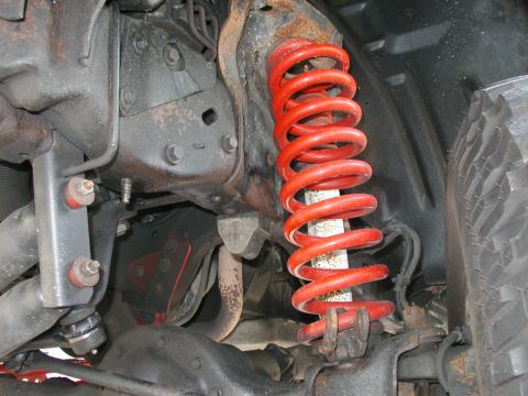 1994 Ford Bronco - Under-fender view of a red lift coil spring seated on a front suspension, with a white-bodied shock inside the coil and a red-bushed steeri…