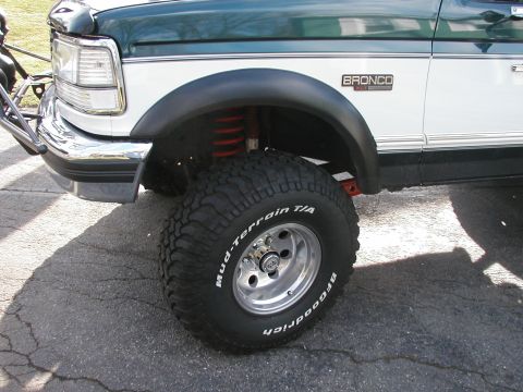 1994 Ford Bronco - Front corner detail of a green-over-white Ford Bronco XLT on cracked asphalt, showing a BFGoodrich Mud-Terrain T/A white-letter tire on a p…