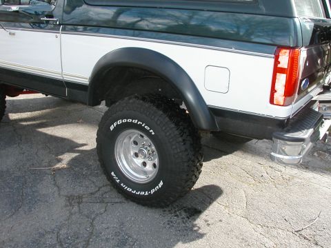 1994 Ford Bronco - Rear quarter detail of a green-over-white full-size Ford Bronco on cracked asphalt, focused on the BFGoodrich Mud-Terrain T/A white-letter…