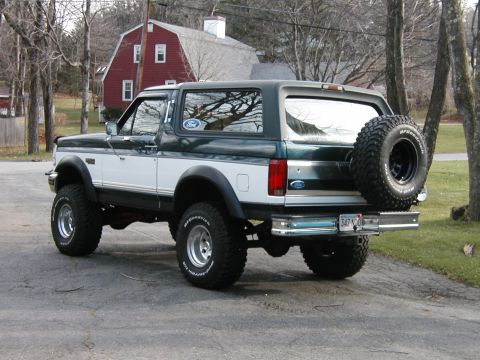 1994 Ford Bronco - This two-tone Ford Bronco is parked on a paved surface with a red barn in the background.