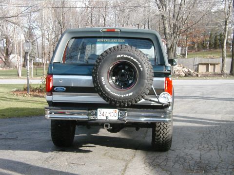 1994 Ford Bronco - The rear of a Ford Bronco is shown parked in a driveway with a spare tire mounted on the tailgate.