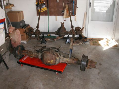 1994 Ford Bronco - Vehicle axles are shown in a garage, with one resting on a red creeper.