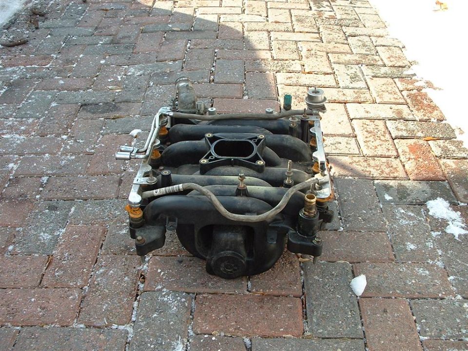 Engine intake manifold sitting on a brick patio with some snow