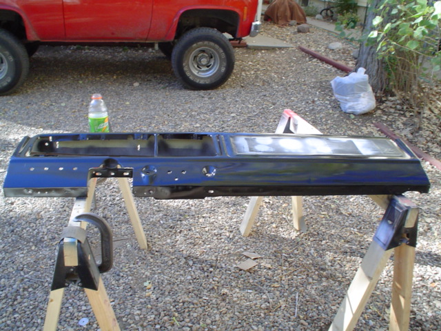 Black-painted truck bed side panel on sawhorses, red square-body pickup behind