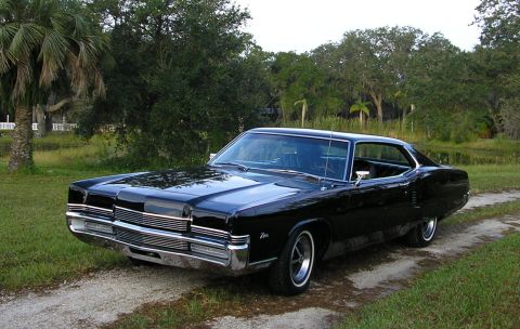 1969 Mercury Marauder - A black 1969 Mercury Marauder is shown from a three-quarter front view, parked on a dirt road with trees and water in the background.