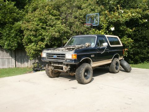 1991 Ford Bronco - A black 1991 Ford Bronco with its hood up and lifted suspension sits on a concrete driveway.