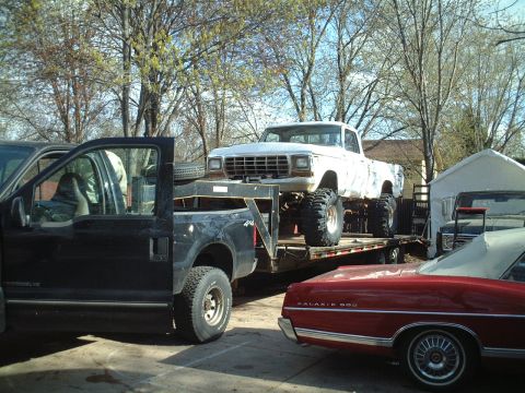 1979 Ford F-150 - A white 1979 Ford F-150 pickup truck is loaded onto a trailer, with other vehicles visible nearby.