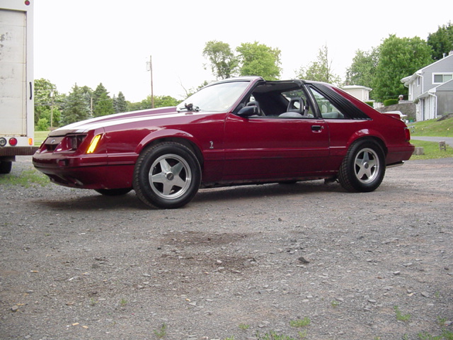 Red coupe with T-tops and a prominent hood scoop parked on a gravel lot
