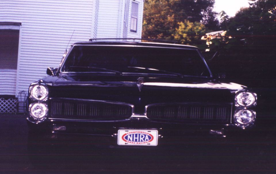 Front of a black 1960s Pontiac with stacked headlights and an NHRA license plate