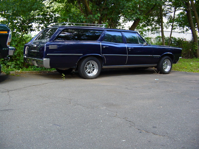 Dark blue classic station wagon parked on cracked asphalt under trees