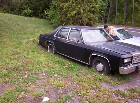 1991 Ford LTD Crown Victoria - A black sedan sits on a grassy shoulder next to another vehicle, with a person leaning into the driver's side window.