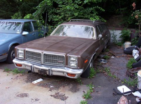 1991 Ford LTD Crown Victoria - A brown station wagon sits in a yard next to another vehicle, with overgrown vegetation surrounding it.