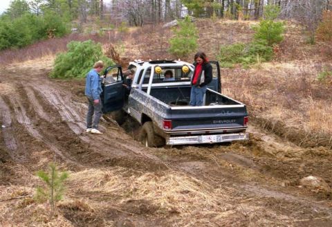 1991 Ford Bronco - A Chevrolet pickup truck is stuck in a muddy trail, with people standing around and inside the vehicle.