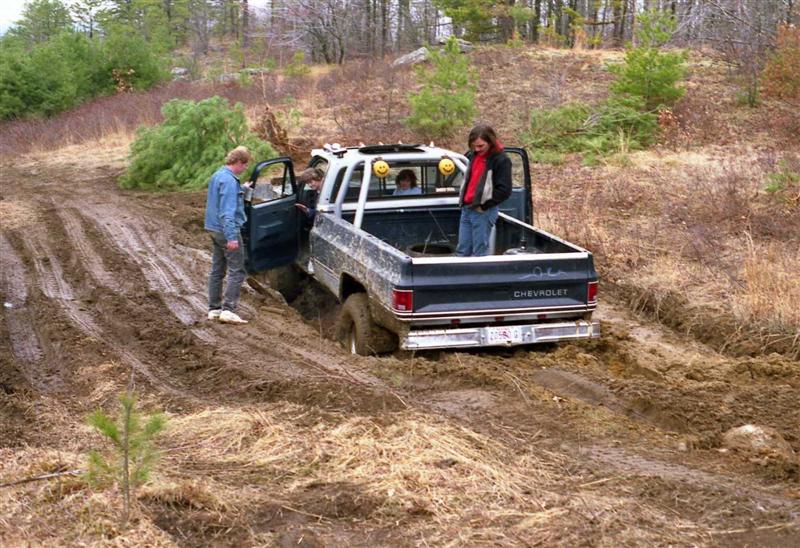 Pickup truck stuck in mud with people around it. A Christmas tree is in the background