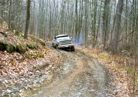 1991 Ford Bronco - Pickup truck navigates a challenging muddy path through a dense forest.