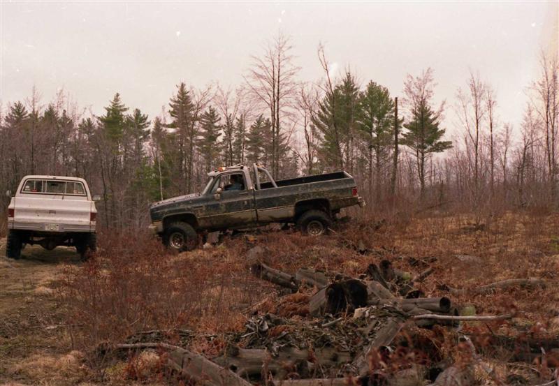 Dark pickup truck navigating rough terrain next to a white pickup truck