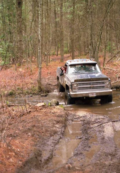 1991 Ford Bronco - This pickup truck is navigating a wet and muddy trail through a wooded area.