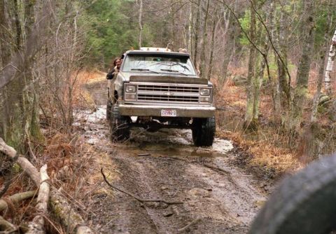 1991 Ford Bronco - A lifted truck navigates a muddy path in a forest setting.