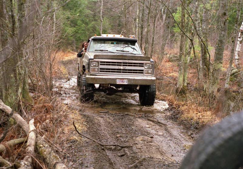 Truck with lifted suspension driving through mud on a wooded trail