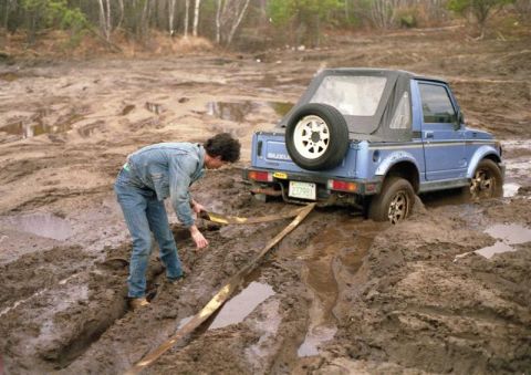 1991 Ford Bronco - A person attempts to free a blue Suzuki Samurai that is stuck deep in mud.
