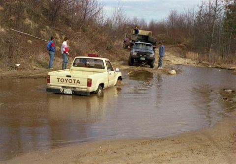 1991 Ford Bronco - A Toyota pickup truck is stuck in a water crossing, with another vehicle attempting to assist.