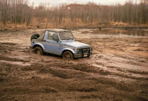 1991 Ford Bronco - This off-road vehicle is deeply mired in a muddy, wet terrain with trees in the background.