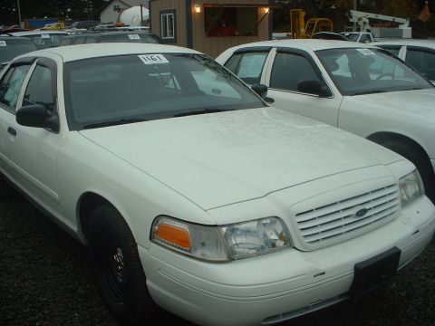 1999 Ford Crown Victoria - A white sedan is parked in a lot with other vehicles, showing its front grille and headlights.