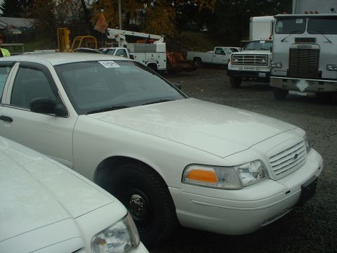 1999 Ford Crown Victoria - White sedan parked in an outdoor lot with other vehicles visible in the background.