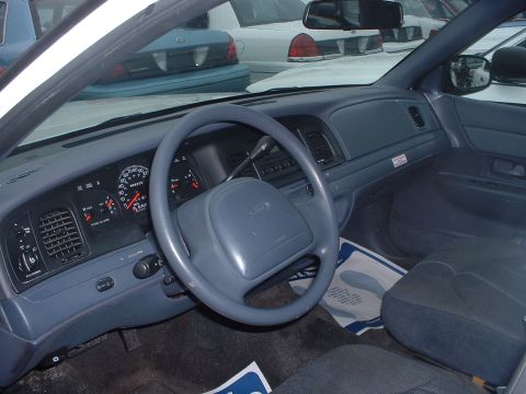 1999 Ford Crown Victoria - The interior of a 1999 Ford Crown Victoria, its dashboard, steering wheel, and seats, with other vehicles visible in the background.
