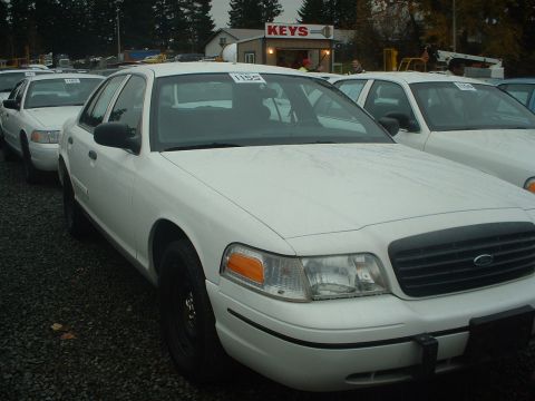 1999 Ford Crown Victoria - Multiple white Ford Crown Victorias are parked in a lot, with a building labeled 'KEYS' in the background.