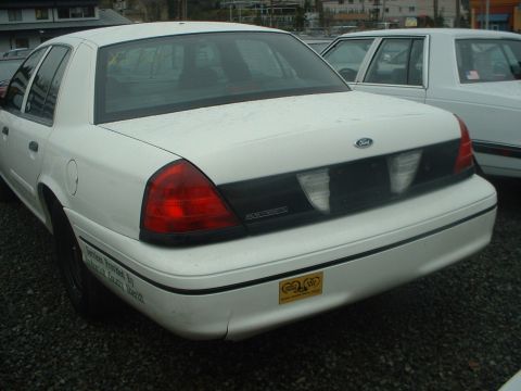 1999 Ford Crown Victoria - A white Ford sedan is seen from the rear, parked next to another vehicle in an outdoor lot.