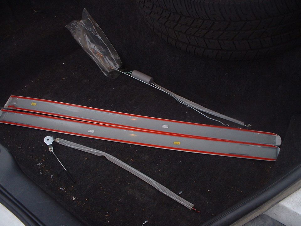 Two gray trim pieces with red edging and yellow stickers lie on a dark carpeted surface next to a tire