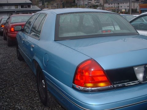 1999 Ford Crown Victoria - Rear quarter view of a blue 1999 Ford Crown Victoria, parked in a lot with other vehicles.