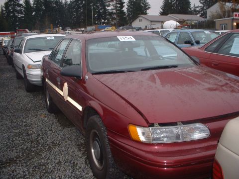 1999 Ford Crown Victoria - Maroon 1996 Ford Taurus with white tape on the door, parked in a car lot.