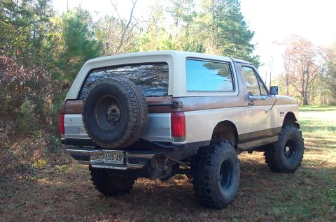 1987 Ford Bronco - This lifted 1987 Ford Bronco is shown from the rear, an external spare tire and a two-tone brown and tan paint scheme.