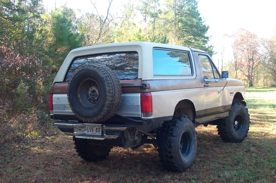 Lifted 1987 Ford Bronco, rear view, with external spare tire and brown/tan paint