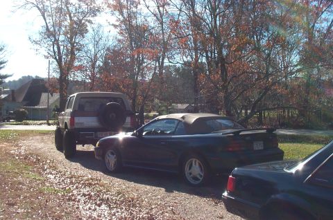 1987 Ford Bronco - A Ford Bronco and a Ford Mustang convertible are parked side-by-side on a gravel lot.