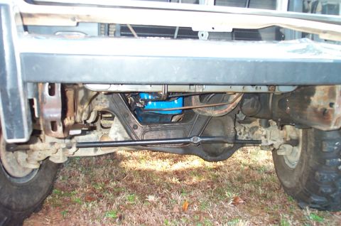 1987 Ford Bronco - Close-up of the front axle and steering components of a vehicle, with a blue oil pan visible.