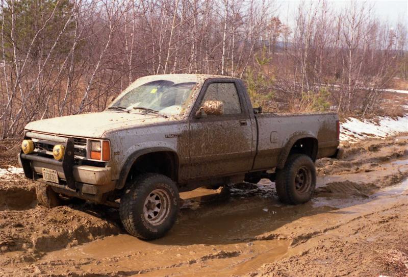 Muddy gray pickup truck navigating a muddy trail with off-road lights