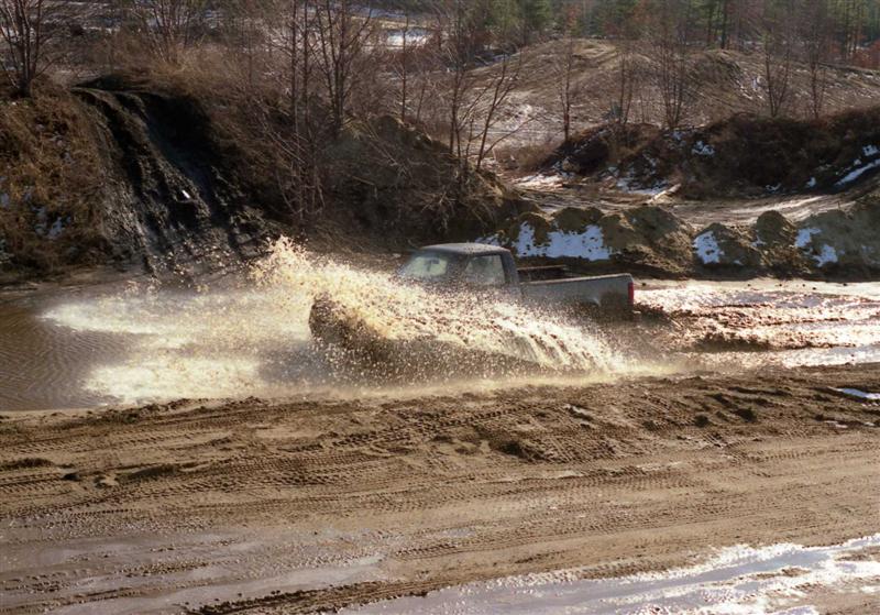 Pickup truck splashing mud while driving through a muddy area