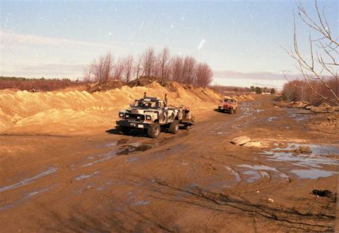 1991 Ford Bronco - A camouflaged pickup truck navigates a muddy terrain with another vehicle in the distance.