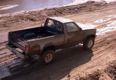 1991 Ford Bronco - A muddy pickup truck navigates a wet, rutted dirt track.