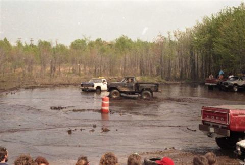 1991 Ford Bronco - Several trucks are stuck or driving through a muddy, waterlogged area, with onlookers watching from the side.