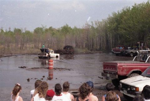 1991 Ford Bronco - Multiple trucks participate in a mud bogging event with onlookers present.