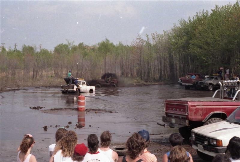 Mud bogging event with several trucks in the mud and spectators watching