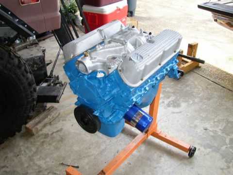 1995 Ford Bronco - A blue engine is mounted on an orange stand, with a blue oil filter attached. A portion of a brown vehicle is visible on the left side of t…