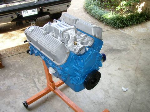 1995 Ford Bronco - A blue engine is displayed on an orange stand, with the rear of a truck visible in the background.