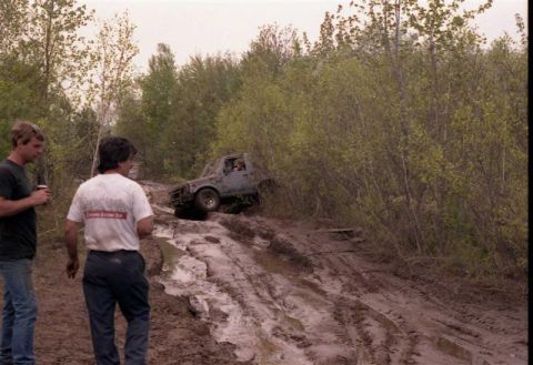 1991 Ford Bronco - Two men observe a Suzuki Samurai navigating a difficult muddy off-road trail.